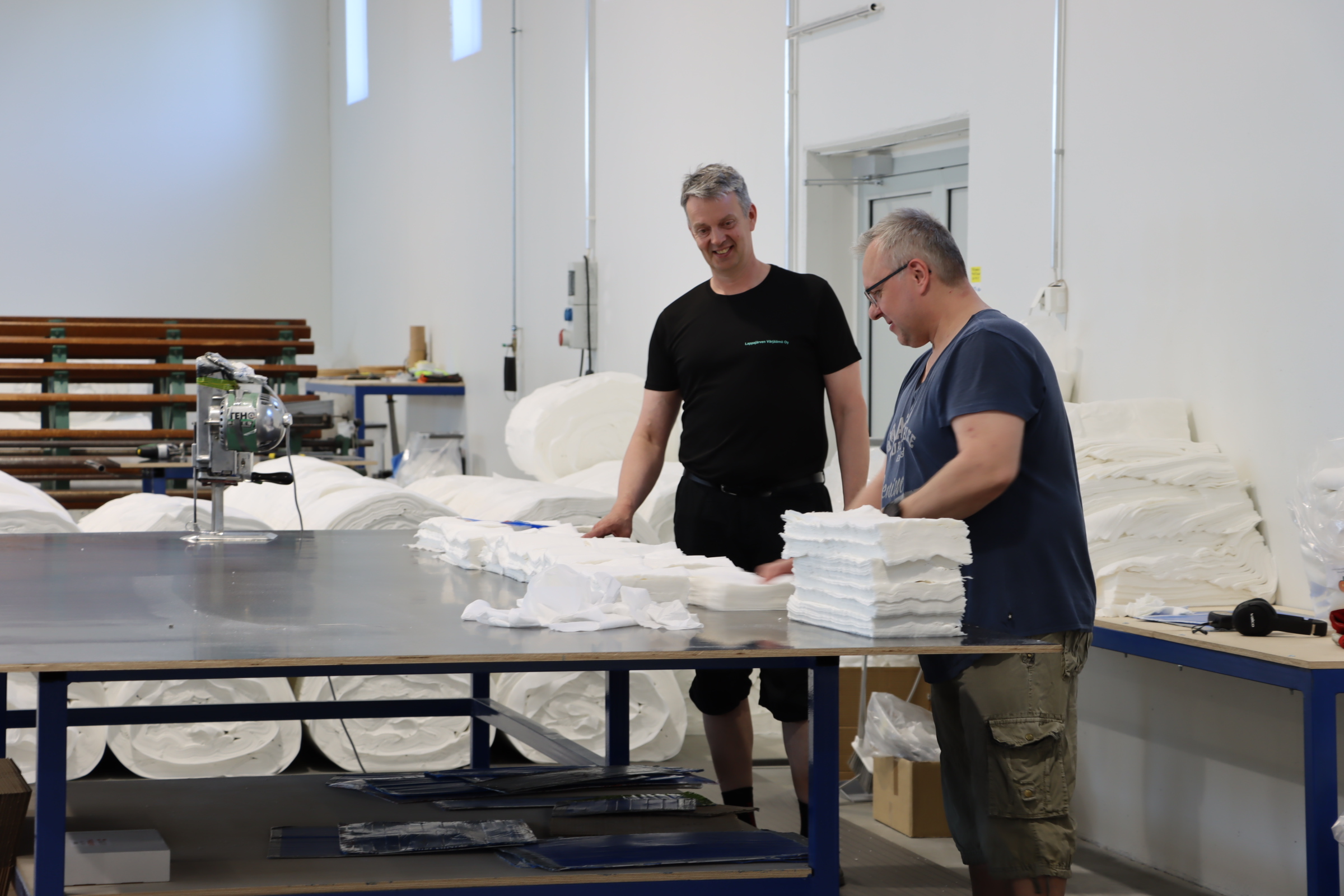 Kaksi henkilöä seisoo tehdas tiloissa pöydän edessä, jossa pyyhkeitä