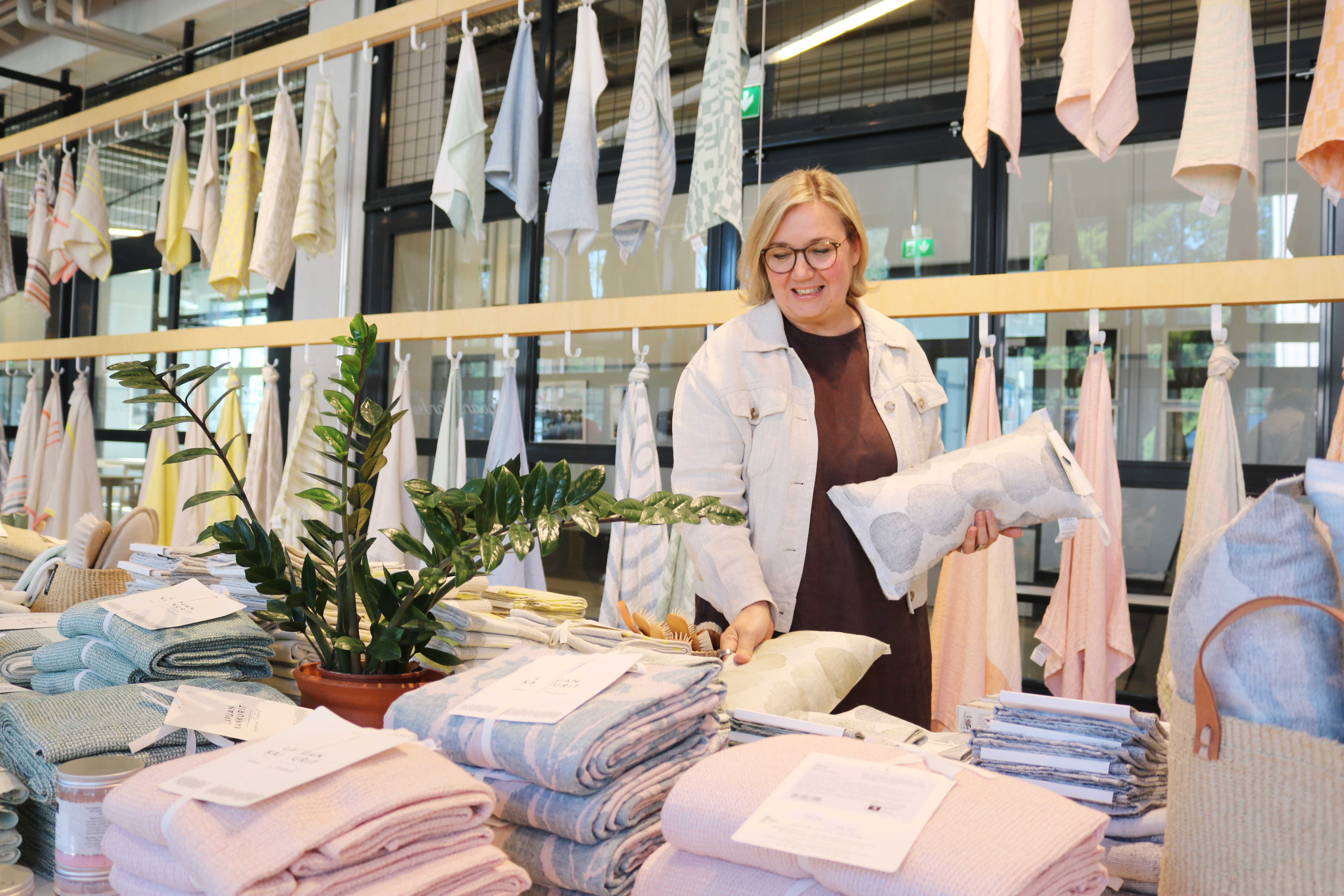 Jaana Hjelt Lapuan Kankureiden myymälässä, jossa taustalla pöydillä ja riippumassa erilaisia pyyhkeitä.