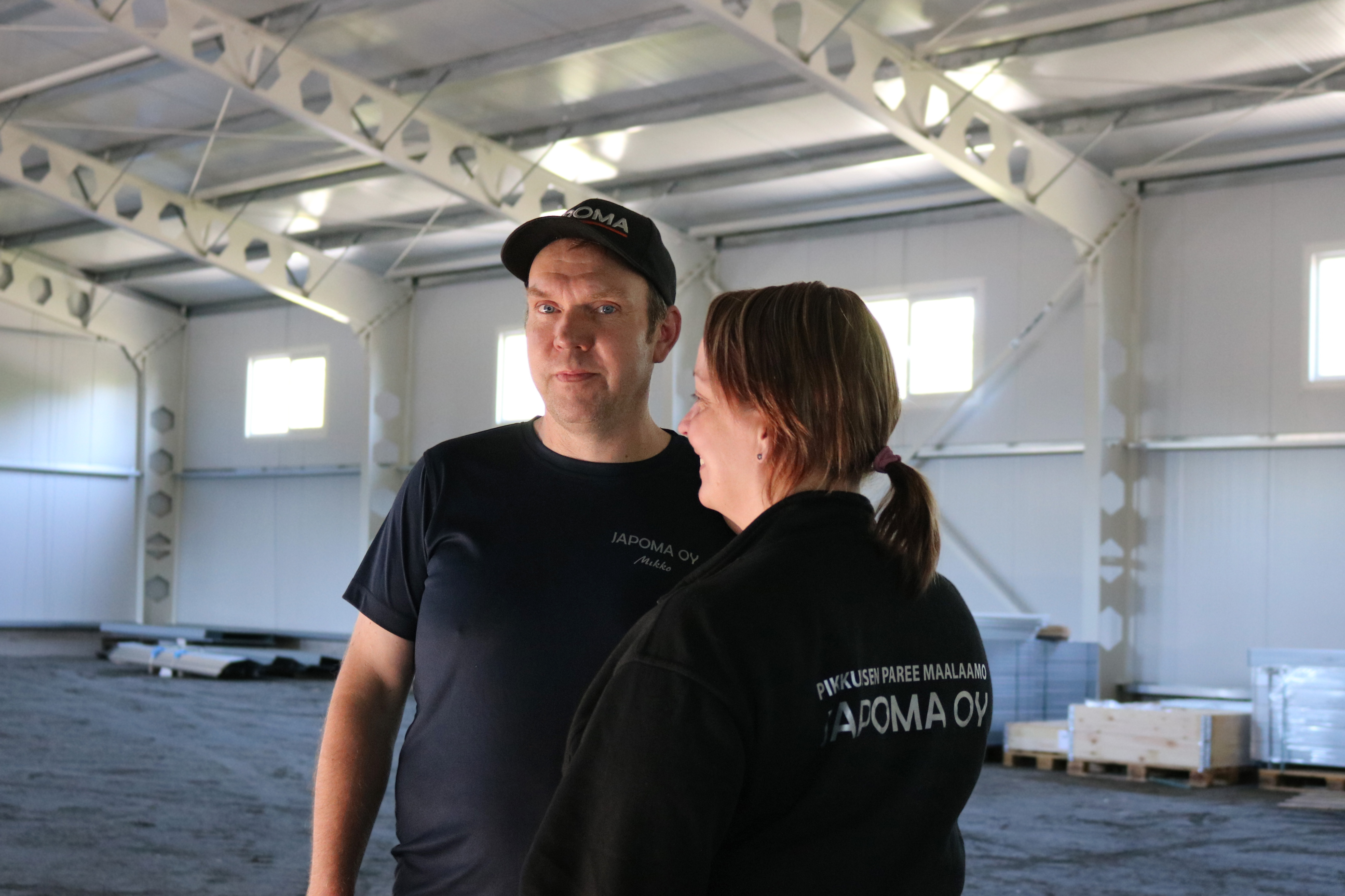 Mikko ja Heidi Kuja-Perälä seisovat aurinkoisessa säässä sisällä Japoma Oy:n tehtaassa.
