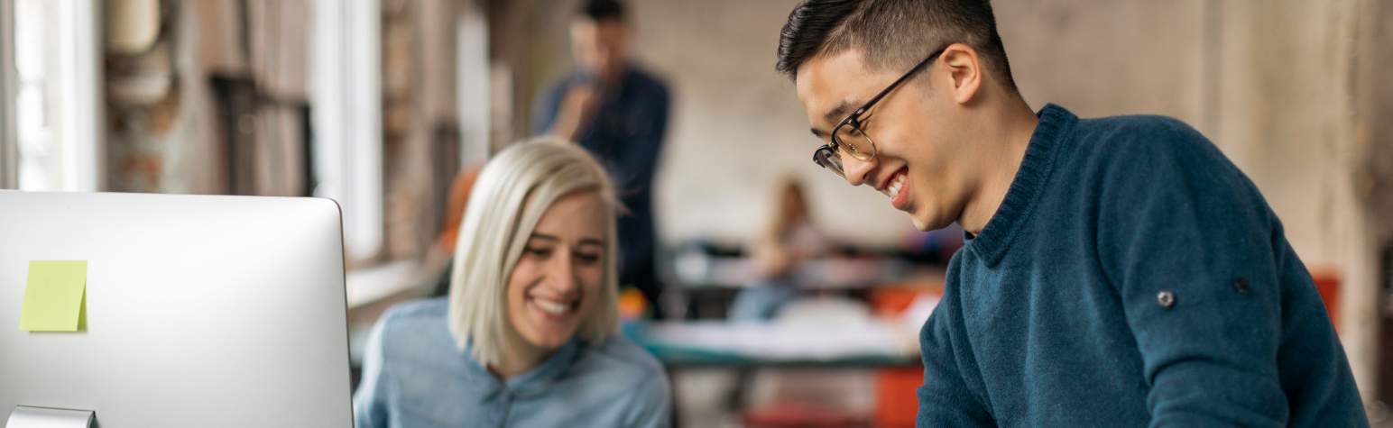 Tämä kuva kuvaa tilannetta huoneessa, jossa on kolme henkilöä. Heidän kasvonsa on peitetty yksityisyyden suojelemiseksi. Huoneessa vallitsee rauhallinen ja keskittynyt ilmapiiri, mikä viittaa työ- tai opiskeluympäristöön. Yksi henkilö on etualalla sinisessä neuleessa ja näyttää työskentelevän jossain kuvan ulkopuolella. Keskellä oleva nainen, jolla on vaaleat hiukset, keskittyy tietokoneen näyttöön, jossa on keltainen muistilappu.